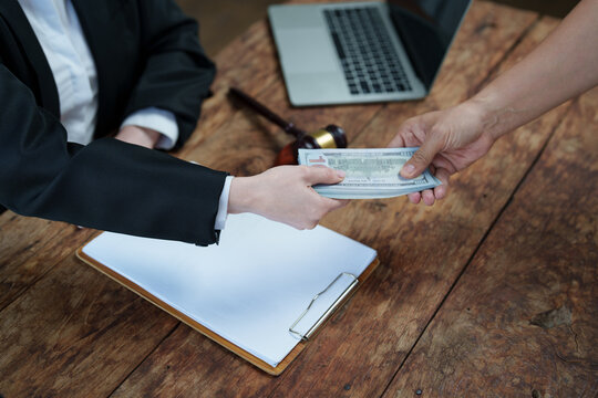 Person in suit accepting cash from another hand across an office desk, symbolizing bribery, corruption and illicit payment in a legal or corporate setting