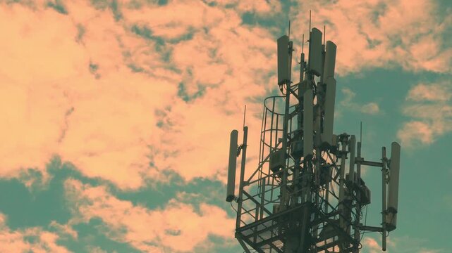 Cell Tower Closeup, Mobile Operator Tower Close-up, Mobile Communications closeup and A Beautiful Time Lapse of Yellow Orange Fluffy Clouds in a Blue Clear Azure Sunset Sky in Sunlight.