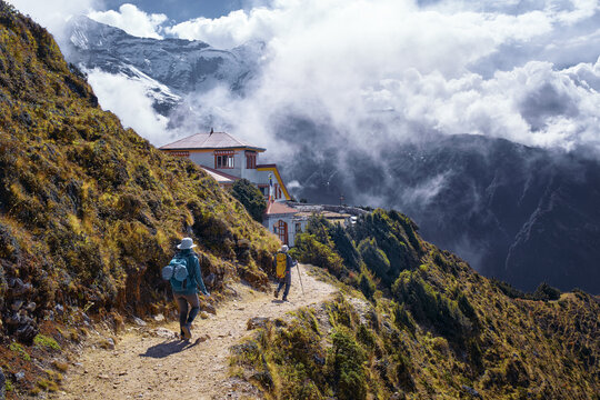 Couple of Trekkers Walking Mountain Path Approaching Teahouse Surrounded by Dramatic Peaks and floating Clouds on Route to Everest Base Camp, Nepal