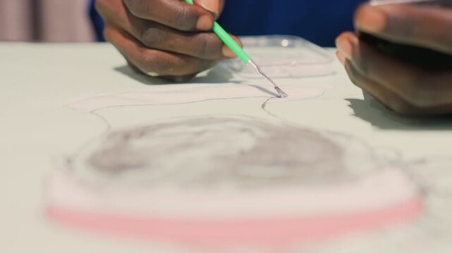 Black hands painting portrait sketch on table, closeup view of artist inking fine lines with green pencil, soft studio light, concentrated process, portrait commission, illustrative study