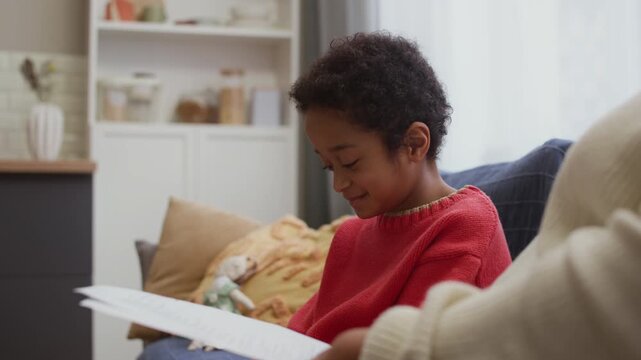 Little African American boy examining papers with grades while they in hands of his grandmother
