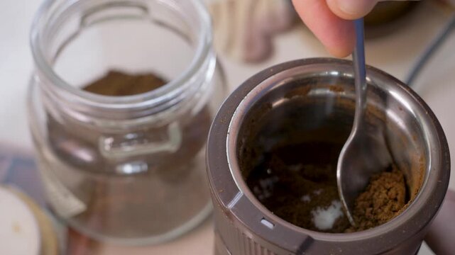 Hand transfers fine coffee powder from grinder into storage jar. Aroma stays intense. Brewed drink to support focus and vitality. Roasted coffee beans are ground down to make coffee