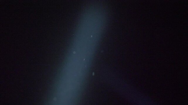 Directed light breaks black sky at night during Ukrainian air threat. Flashlight searches UAV drone silhouette above sleeping city. Defense readiness during war aggression