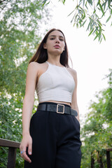 Fototapeta premium Young woman with long dark hair posing outdoors, looking directly at the camera. Minimalist fashion and natural beauty concept. Lifestyle portrait.