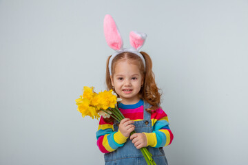 A cute little girl with bunny ears holds a bouquet of spring flowers on a white background with...