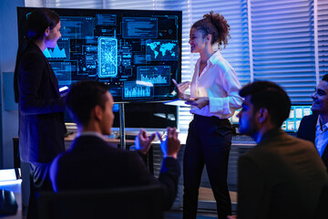Obraz premium Professional IT team analyzing global network security dashboard in modern control center. Female manager leading cyber technology project discussion in dark night office.