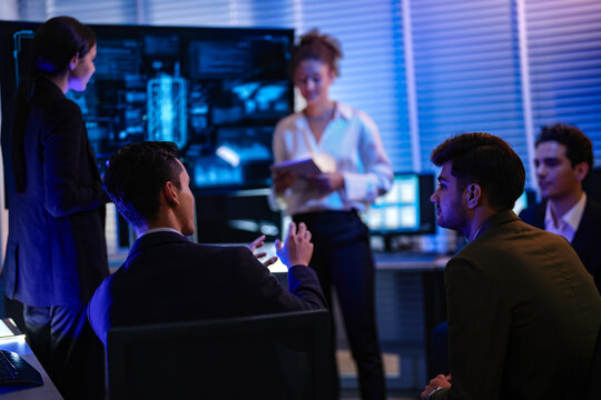 Confident businesswoman presenting global data analysis to team on large digital screen. Professional executive leading IT strategy meeting in modern blue light night office.