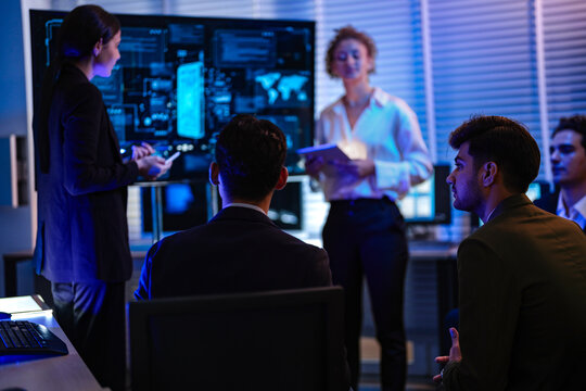 Professional IT team analyzing global network security dashboard in modern control center. Female manager leading cyber technology project discussion in dark night office.