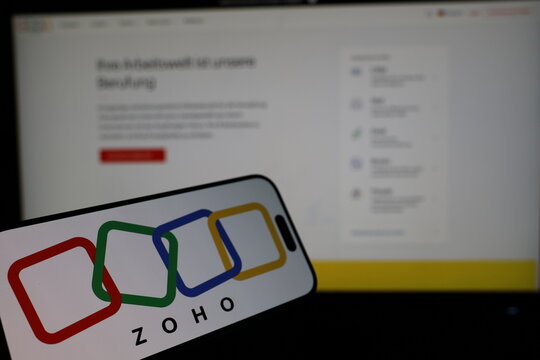 Kiel, Germany - 02-27-2026: Smartphone displaying Indian software company Zoho logo in front of companys webpage