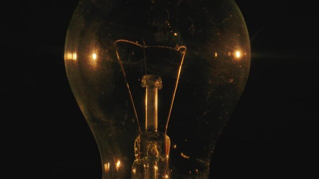 Close up shot of an old fashioned light bulb with visible filament against a dark backdrop, emphasizing its classic design.