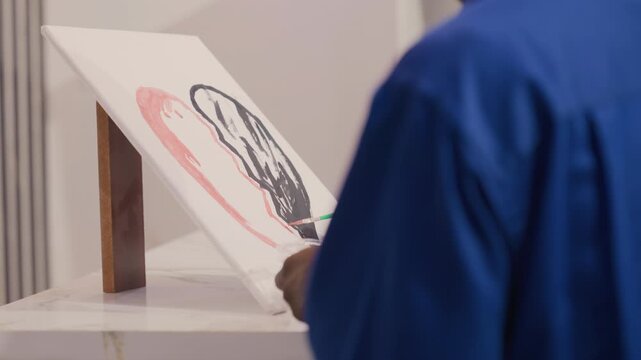 Black artist reviewing canvas composition, back view of black painter in blue smock studying pink stroke and black silhouette on easel, studio lighting, reflective pause and planning next movement,