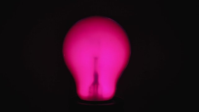 A warmly glowing light bulb that changes colors against a dark background. Captures the essence of innovation and warmth.