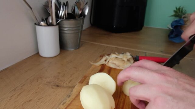 Man chops new potatoes on wooden cutting board on kitchen counter