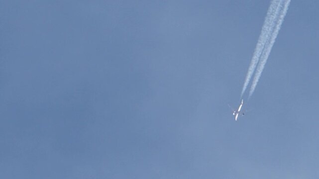 Tracking jet airliner flying through blue sky leaving white chemtrails