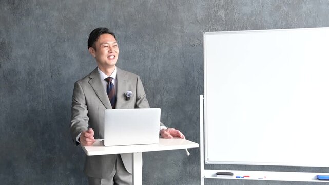 ピンマイクをつけてプレゼンをするスーツの日本人男性