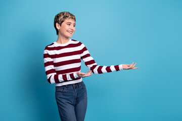 Young woman in striped sweater stands against blue background smiling and presenting fashion...