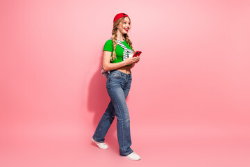 Young stylish girl with braids in a green top jeans and cap smiles while using a phone against a...