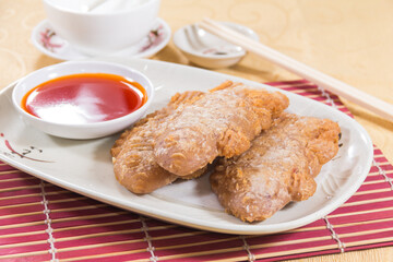 A white plate with two golden deep-fried taro dumplings served with a small bowl of chili dipping sauce.
