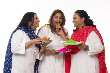 Indian Women Holi Celebrations. Three friends eating Gujiya sweets and holding full plate of color...