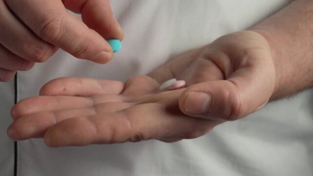 Hands of a person in a white coat holding a blue pill above an open palm with a pink pill resting inside, showcasing careful selection process