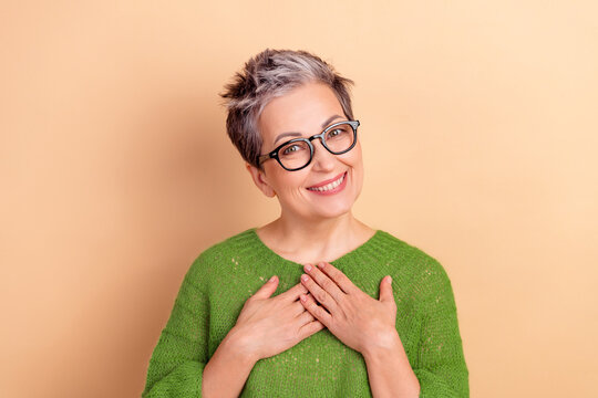 Smiling mature lady with green sweater and glasses standing against beige background for stock ad and lifestyle use
