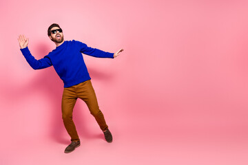 Young man in blue pullover dances playfully against pink background exuding joy and style