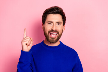 Fototapeta premium Happy young man in blue sweater smiles and points upward against pink background for lifestyle and fashion promotion