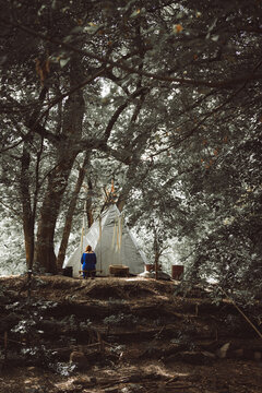 white wigwam teepee tent in a lush forest with a loneliness person sitting nearby
