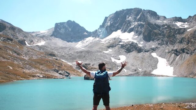 A traveler in a white T-shirt solemnly makes a helpless gesture near a mountain lake on the top of a mountain