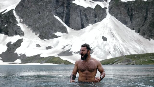 A man with a beard swims and screams in an ice lake in the highlands