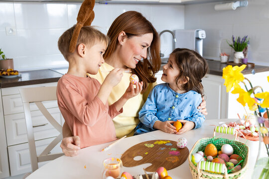 Smiling Mother Painting Easter Eggs with Two Children at Home