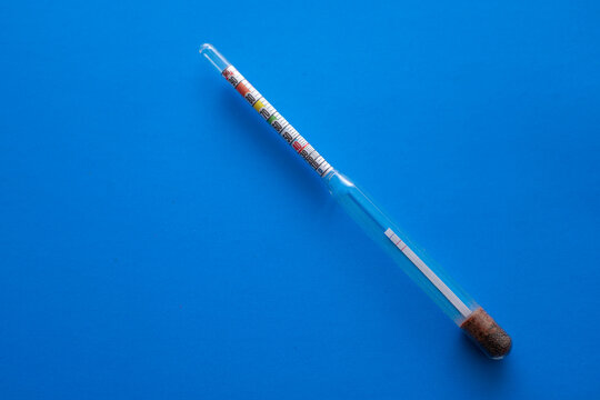 ​A glass hydrometer with a colored scale is positioned diagonally on a deep blue background. This laboratory device provides accurate measurement of liquid density and alcohol strength,