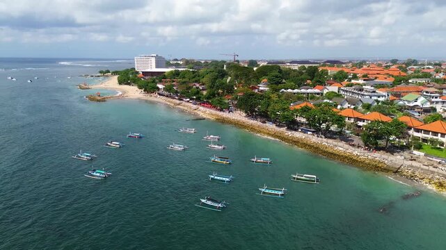 Aerial drone video of Sanur Beach in Bali, Indonesia, featuring cruise ships and boats anchored near the shoreline with luxury resorts along the tropical coastline. 