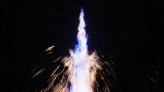Mesmerizing upward view of a vertical blue and gold firework against a black background with sparkling effects