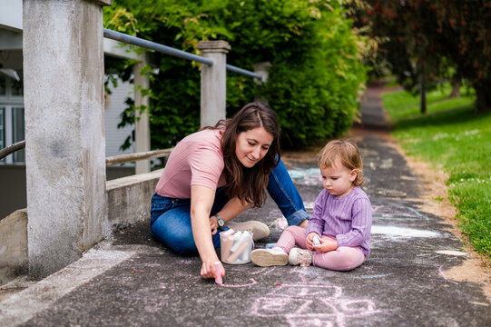 Mum and toddler daughter sitting on a pavement making drawings with colourful chalk