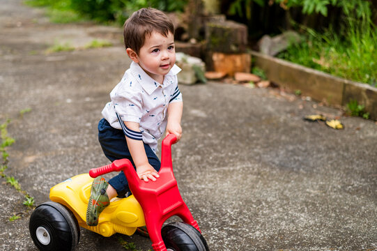 Young boy getting off red and yellow tricycle outside in garden space
