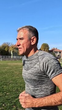 Active 54-Year-Old Fit Man Jogging on Grass Sports Field on a Sunny Day. Series Track Code: Fit-Mature-Man-54-Outdoor-Fitness-Series-2024 . Explore the full collection to find matching shots.