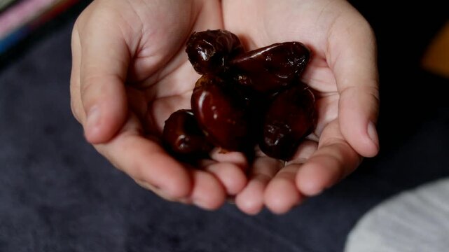 A close-up video of two hands cupping several dates and gently letting them fall one by one. The scene highlights traditional food handling and the natural texture of dates, suitable for themes relate