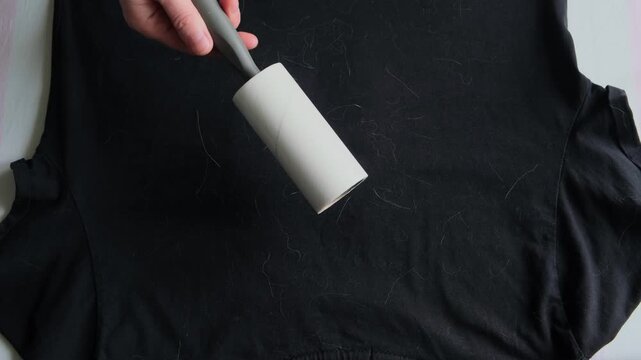 Close-up hand of a woman using lint roller to clean black t-shirt.