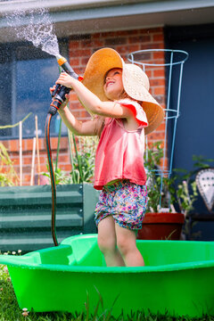 Little girl playing outdoors with hose in backyard wearing big floppy sun hat - water play