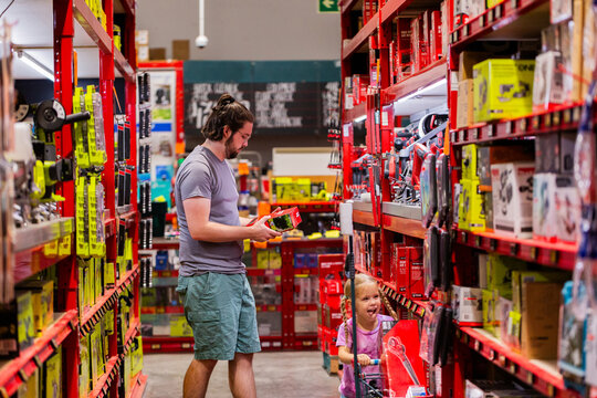 Dad shopping with daughter choosing product to purchase off shelf in hardware store shop