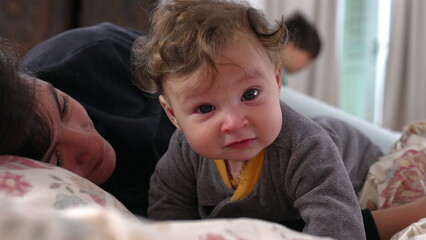 Fototapeta premium Baby looking directly at camera with curious expression while mother lies beside, engaged and observant, cozy family moment, intimate indoor bonding, early child development