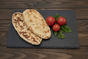 Warm traditional flatbread with toasted crust served with fresh tomatoes, herbs and thick tomato sauce. Rustic food presentation.