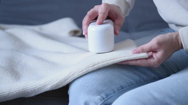Woman using electric fabric shaver removing pills from sweater