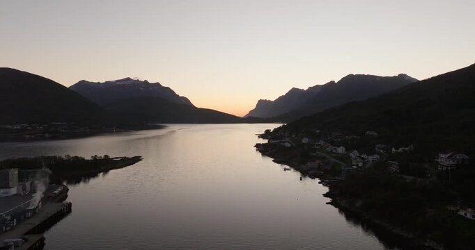 Drone view of Kvaloya island and mountains silhouetted by a golden sunset over a fjord in Tromso, Norway. Aerial forward, copy space