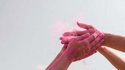 Hands tossing pink powder during Holi celebration, colorful powder flying in the air as people engage in joyful festival.