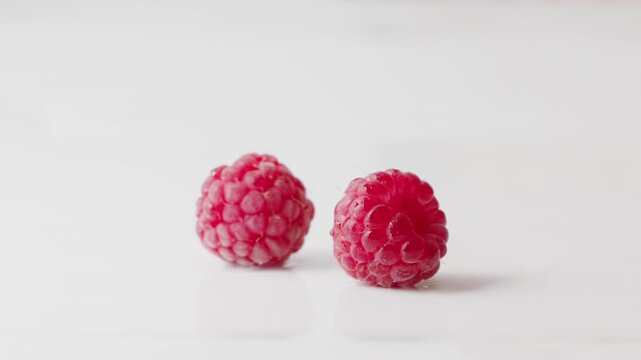 Two perfect, ripe raspberries sit side-by-side on a clean white surface, isolated and detailed.