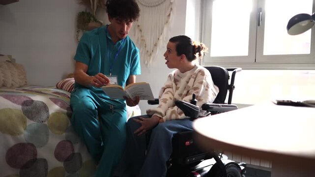 Dedicated young male nurse reading a book aloud to a disabled woman sitting in an electric wheelchair in her room, providing care, support, and companionship during rehabilitation