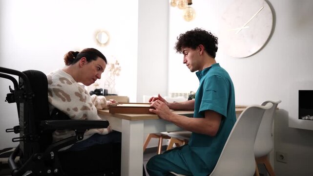 Attentive male caregiver engaging a woman with cerebral palsy in a therapeutic board game session, supporting her rehabilitation and cognitive stimulation in a home care setting