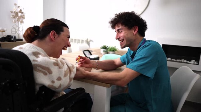 Young male caregiver helping a laughing disabled woman in a wheelchair with her glucose monitoring test, providing empathetic and professional home care assistance for managing diabetes